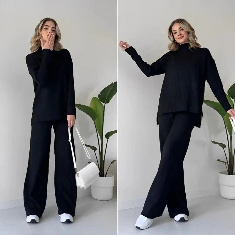 Donna in abbigliamento casual nero, maglione e pantaloni larghi, con borsa bianca e scarpe da ginnastica, davanti a piante d'appartamento.