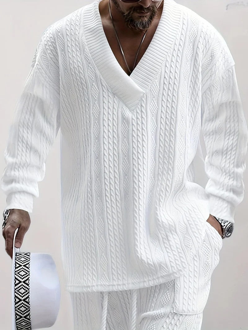 Uomo con maglione bianco a trecce, scollo a V profondo, tiene cappello bianco con fascia decorativa. Moda maschile elegante e casual.