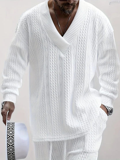 Uomo con maglione bianco a trecce, scollo a V profondo, tiene cappello bianco con fascia decorativa. Moda maschile elegante e casual.