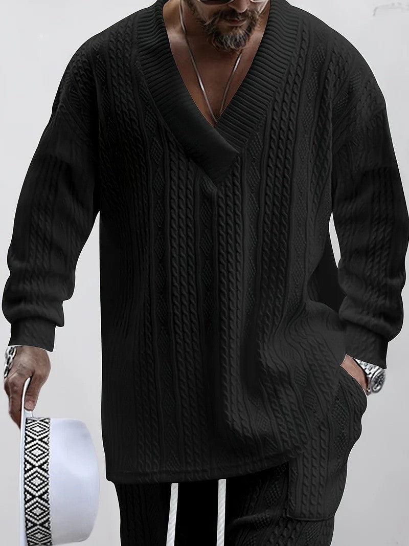 Uomo con maglione nero a maglia grossa, scollo a V, tiene cappello bianco. Moda maschile elegante, abbigliamento invernale casual.