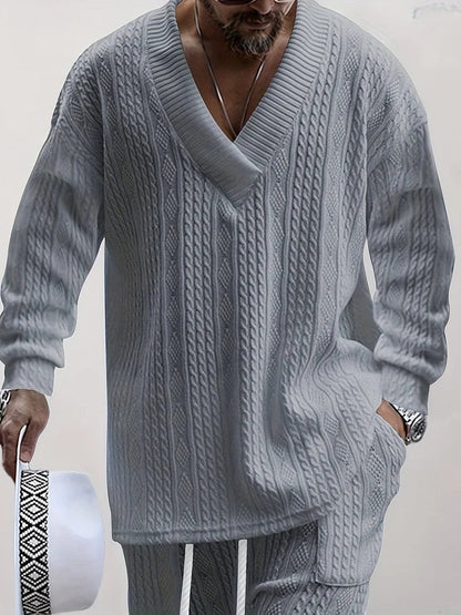 Maglione uomo grigio a maglia grossa con scollo a V, abbinato a pantaloni coordinati. Stile casual elegante, moda maschile autunnale.