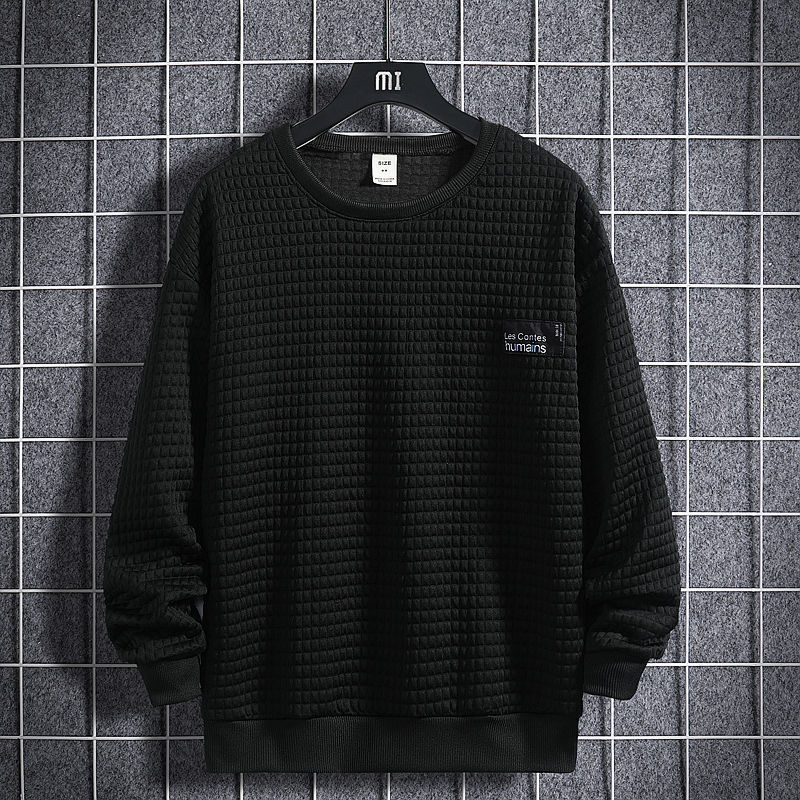 Maglione nero a trama quadrettata su sfondo grigio a griglia, appeso su gruccia. Design casual, ideale per moda autunnale e invernale.