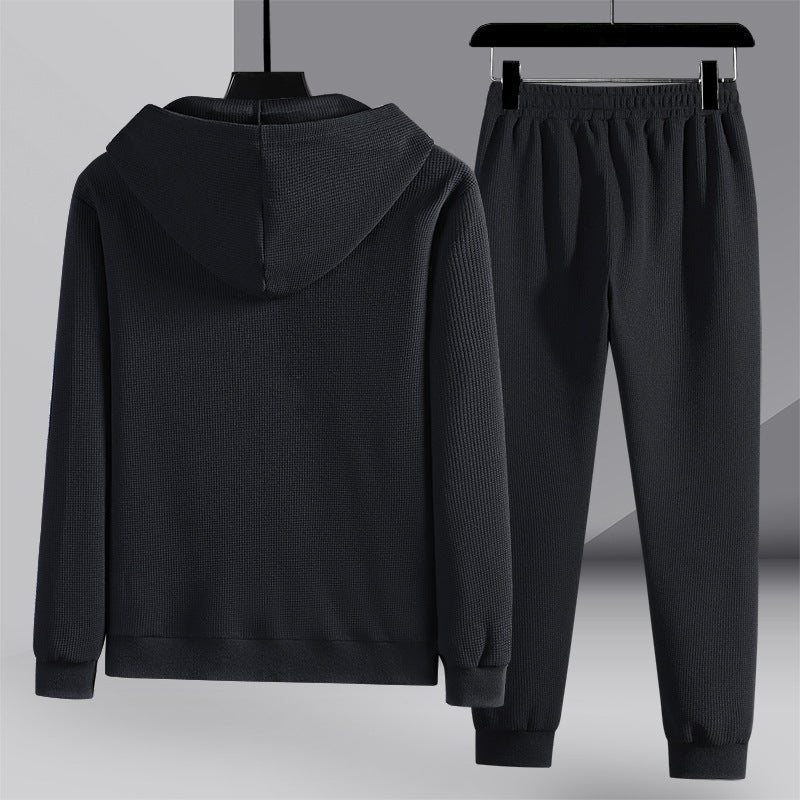Tuta sportiva nera con cappuccio, composta da felpa e pantaloni, appesa su grucce. Abbigliamento casual, moda uomo, tessuto a coste.