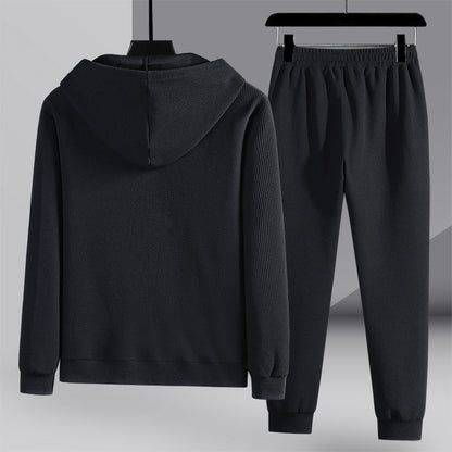 Tuta sportiva nera con cappuccio, composta da felpa e pantaloni, appesa su grucce. Abbigliamento casual, moda uomo, tessuto a coste.