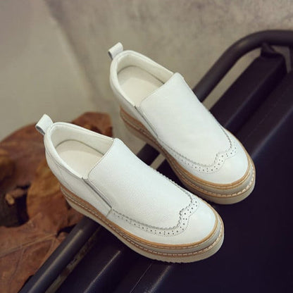 Scarpe slip-on bianche in pelle con suola in gomma marrone, dettagli brogue, su sfondo neutro. Calzature eleganti e comode per ogni occasione.