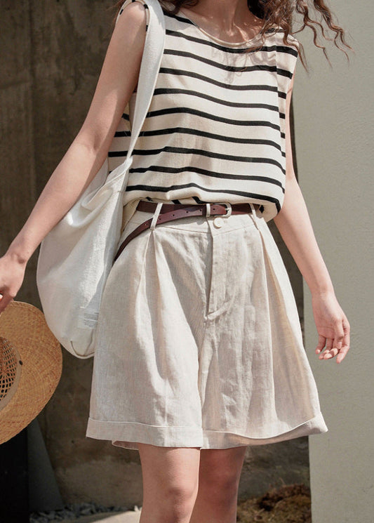 Donna con top a righe bianche e nere, pantaloncini beige, cintura marrone e borsa bianca. Moda estiva casual, look fresco e rilassato.