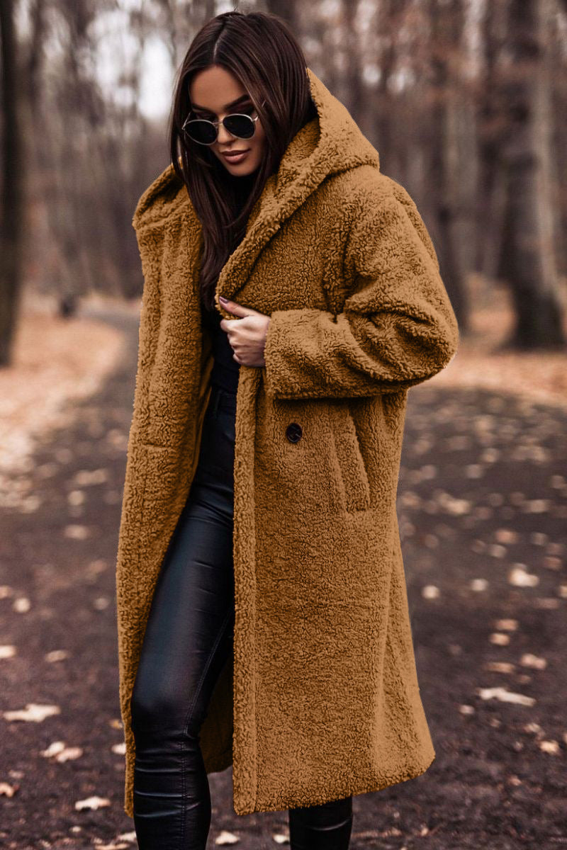 Donna con cappotto teddy marrone, occhiali da sole neri, pantaloni in pelle nera, passeggia in un parco autunnale. Moda autunno inverno.
