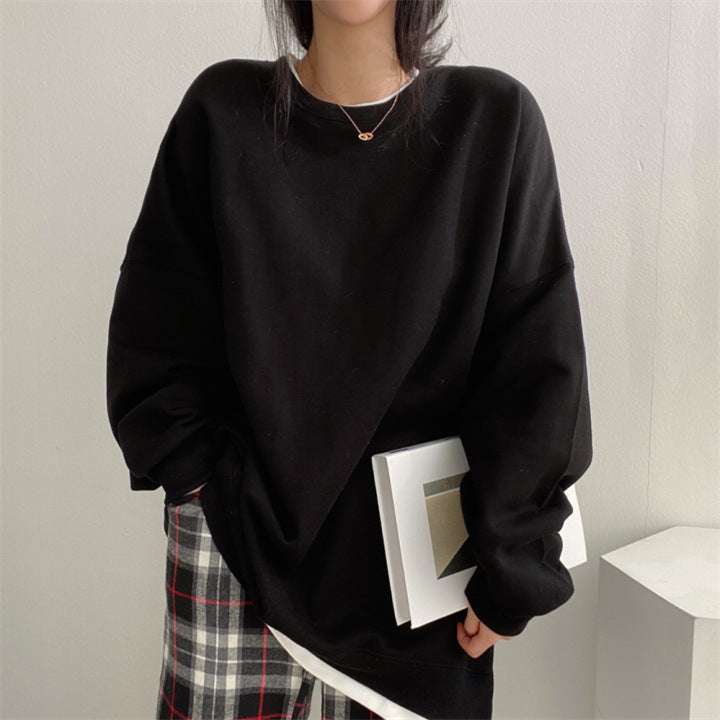 Donna con maglione nero oversize, pantaloni a quadri, tiene un libro bianco. Moda casual autunnale, stile minimalista, outfit comodo.