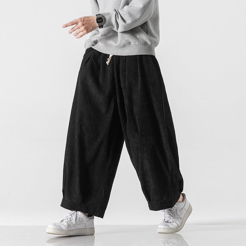 Pantaloni larghi neri a coste, indossati con felpa grigia e sneakers bianche. Moda casual uomo, stile streetwear contemporaneo.