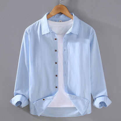 Camicia azzurra da uomo su gruccia, con bottoni marroni e maniche arrotolate, sopra una maglietta bianca. Moda casual, abbigliamento maschile elegante.