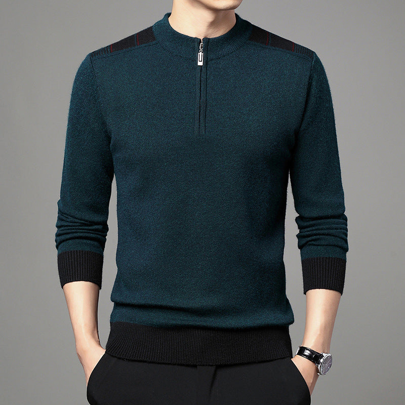Maglione uomo verde scuro con zip corta, dettagli neri sulle spalle, polsini e orlo a coste, indossato con pantaloni neri. Moda maschile elegante.