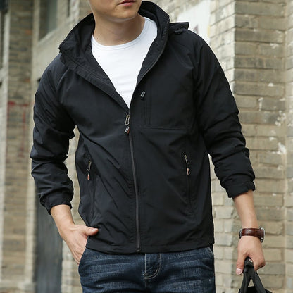 Uomo con giacca nera casual, zip frontale, mani in tasca, jeans blu, sfondo di mattoni. Moda maschile, abbigliamento autunnale, stile urbano.