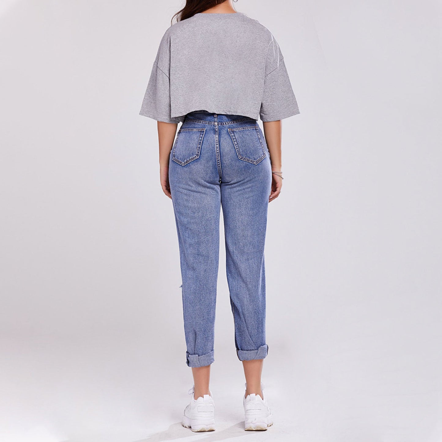 Donna di spalle con maglietta grigia oversize e jeans a vita alta, scarpe da ginnastica bianche. Moda casual, abbigliamento comodo, stile urbano.