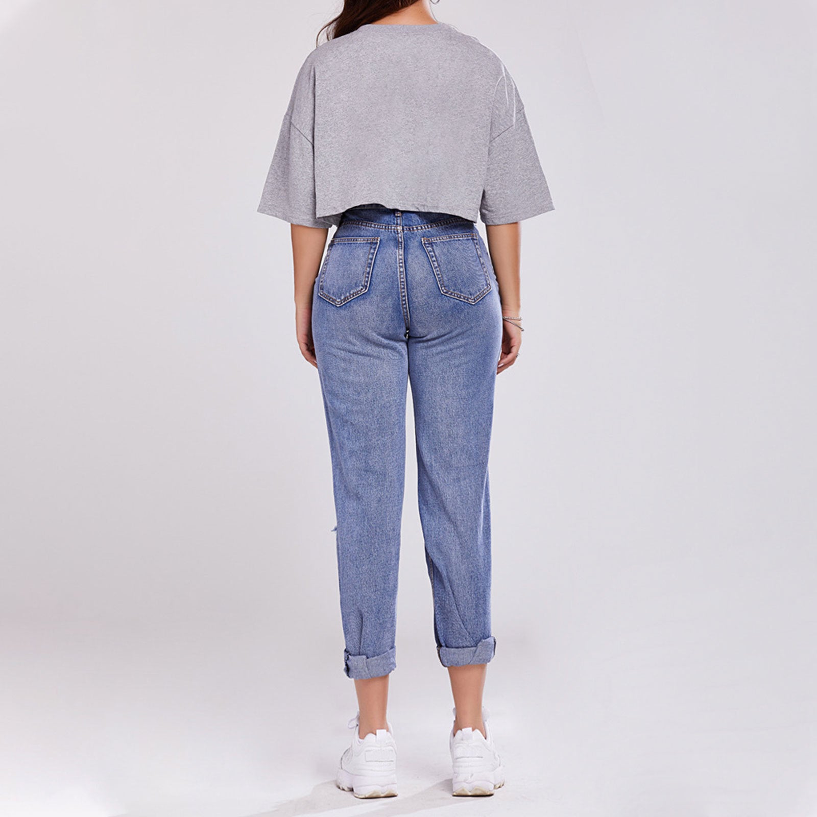 Donna di spalle con maglietta grigia oversize e jeans a vita alta, scarpe da ginnastica bianche. Moda casual, abbigliamento comodo, stile urbano.