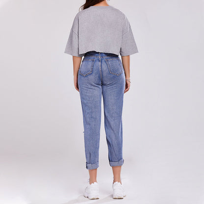 Donna di spalle con maglietta grigia oversize e jeans a vita alta, scarpe da ginnastica bianche. Moda casual, abbigliamento comodo, stile urbano.