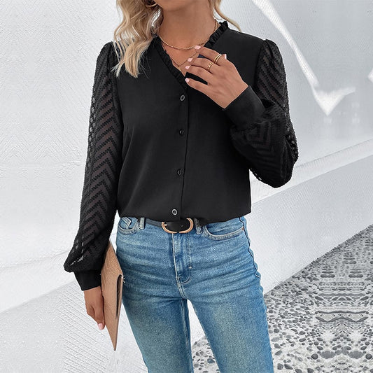 Donna con camicia nera a maniche lunghe trasparenti e jeans blu, accessoriata con cintura nera e borsa beige. Moda casual elegante.