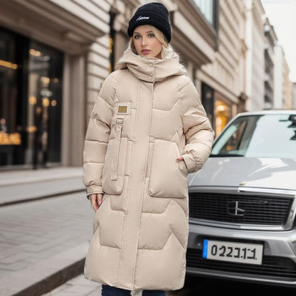 Donna con cappotto imbottito beige e berretto nero, in piedi accanto a un'auto grigia su una strada cittadina. Moda invernale urbana.
