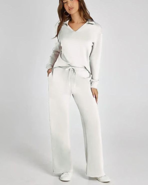 Donna in tuta bianca elegante, con pantaloni larghi e maglia a maniche lunghe, posa su sfondo neutro. Moda casual chic, abbigliamento comodo.