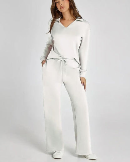 Donna in tuta bianca elegante, con pantaloni larghi e maglia a maniche lunghe, posa su sfondo neutro. Moda casual chic, abbigliamento comodo.