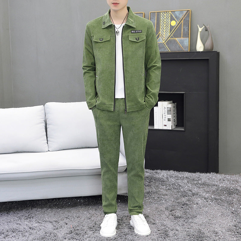 Completo uomo verde in velluto, giacca e pantaloni abbinati, su sfondo salotto moderno con divano bianco e tappeto grigio. Moda casual elegante.