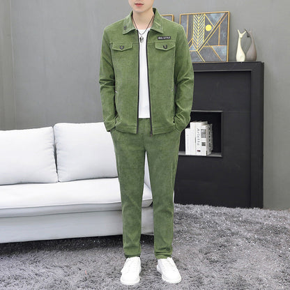 Completo uomo verde in velluto, giacca e pantaloni abbinati, su sfondo salotto moderno con divano bianco e tappeto grigio. Moda casual elegante.