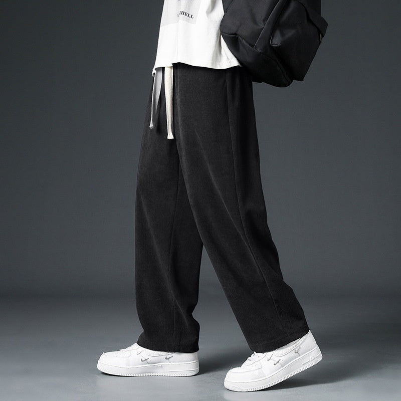 Pantaloni neri larghi da uomo, stile casual, abbinati a scarpe bianche e zaino nero. Moda streetwear, abbigliamento urbano trendy.
