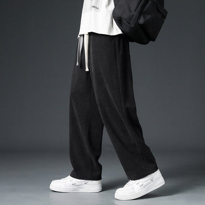 Pantaloni neri larghi da uomo, stile casual, abbinati a scarpe bianche e zaino nero. Moda streetwear, abbigliamento urbano trendy.