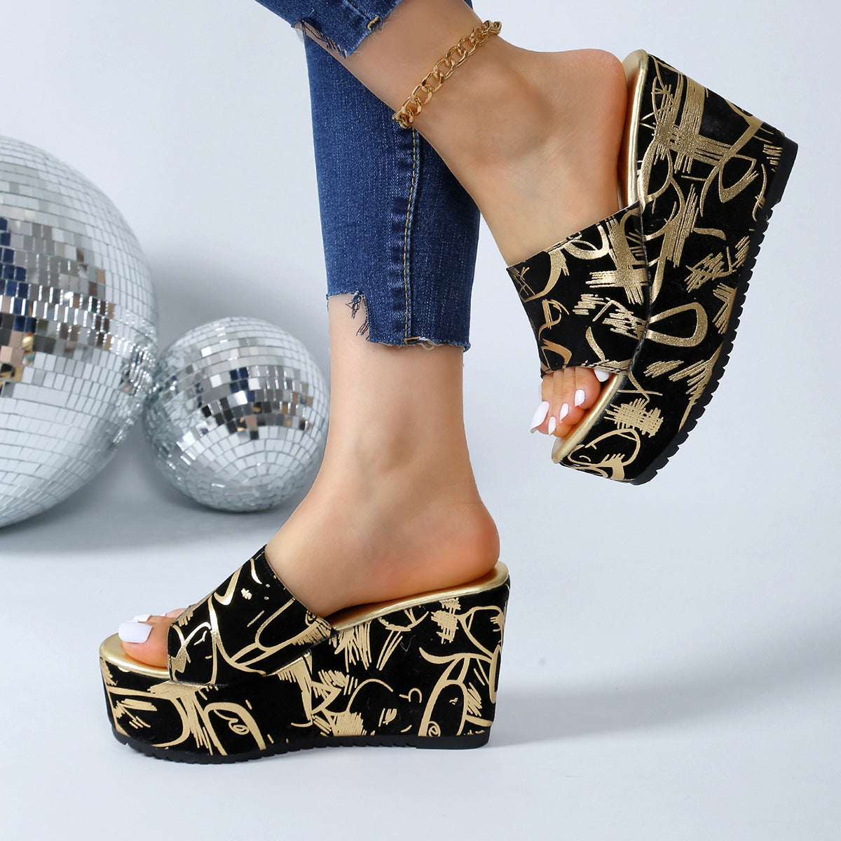 Sandali con zeppa neri e oro con motivo astratto, indossati con jeans aderenti. Scarpe estive eleganti, moda donna, tendenza calzature 2023.