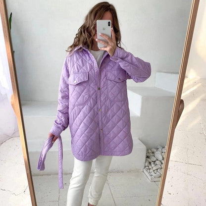 Donna con giacca trapuntata viola, pantaloni bianchi, scatta selfie allo specchio in stanza minimalista. Moda autunnale, abbigliamento casual chic.