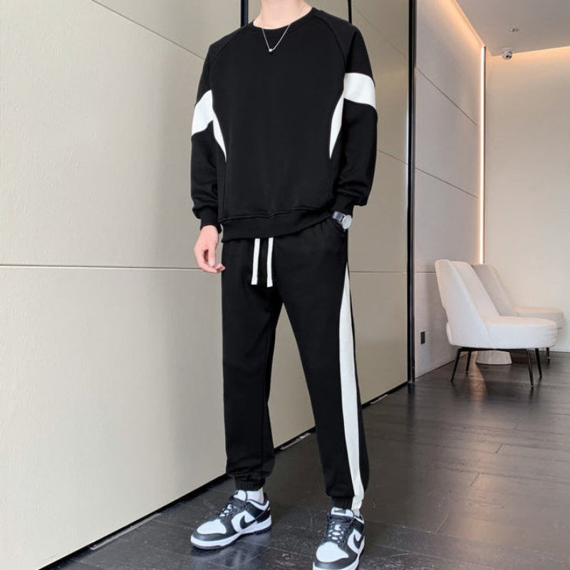Uomo in tuta sportiva nera con strisce bianche, scarpe da ginnastica bianche e nere, in un moderno interno minimalista con poltrona bianca.