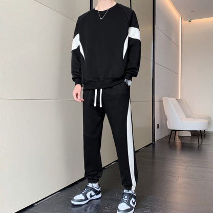 Uomo in tuta sportiva nera con strisce bianche, scarpe da ginnastica bianche e nere, in un moderno interno minimalista con poltrona bianca.