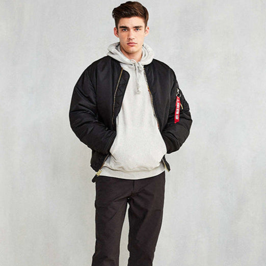 Giovane uomo con giacca bomber nera e felpa grigia, posa casual. Moda maschile, abbigliamento streetwear, stile urbano.