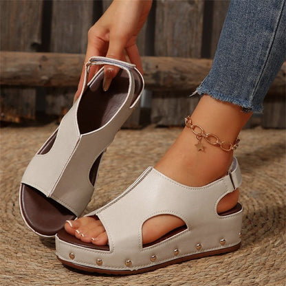 Sandali estivi bianchi con zeppa e borchie, indossati con jeans. Design aperto, cinturino alla caviglia, perfetti per look casual e alla moda.