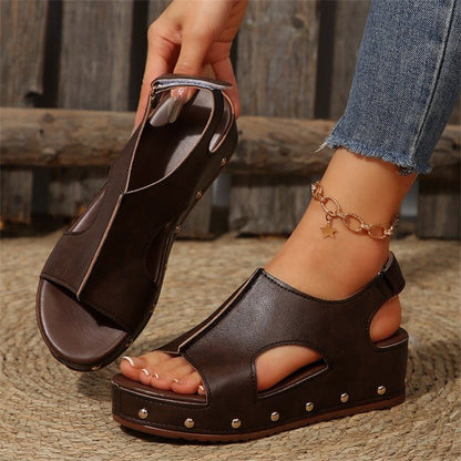 Sandali platform marroni in pelle con borchie, indossati con jeans. Design aperto, cinturino alla caviglia, stile casual estivo.