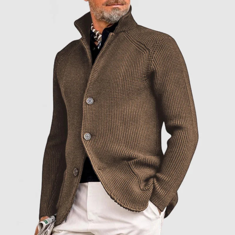 Giacca uomo marrone elegante in maglia, con bottoni, indossata su camicia nera e pantaloni bianchi. Moda maschile autunnale, stile casual chic.