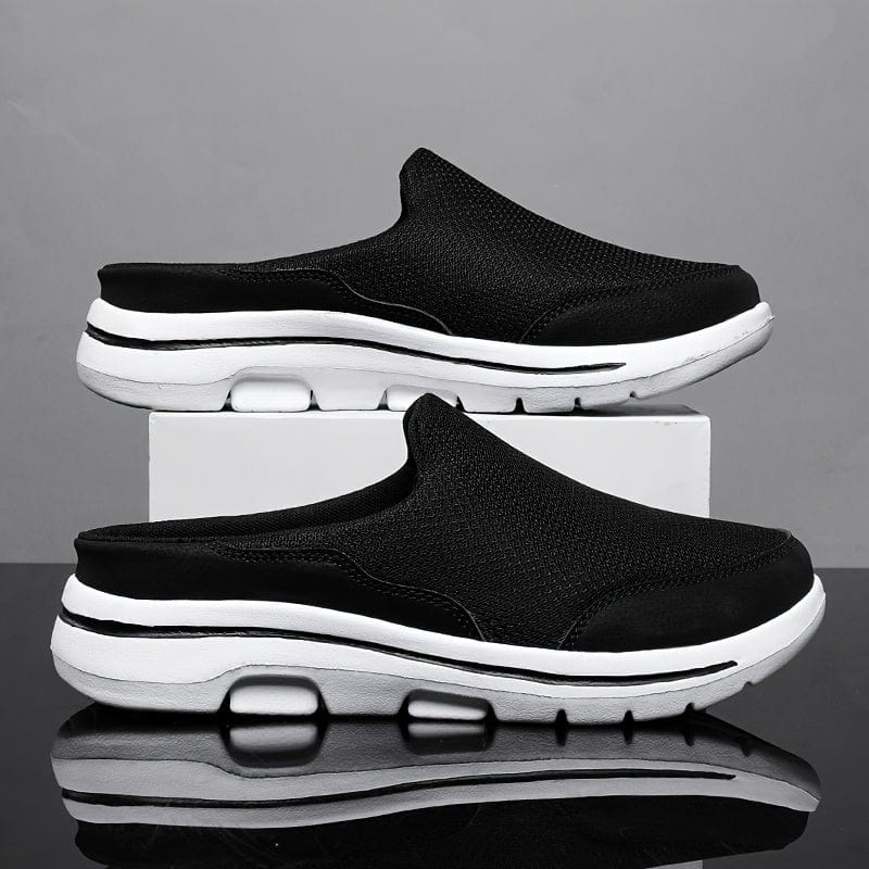Scarpe slip-on nere da uomo su sfondo grigio, suola bianca ammortizzata, design casual e sportivo, ideali per comfort e stile quotidiano.