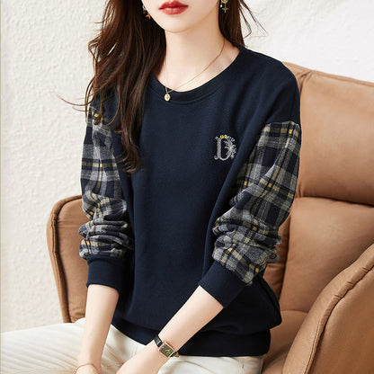 Donna con maglia blu scuro, maniche a quadri, seduta su divano beige. Moda casual, abbigliamento autunnale, stile elegante.