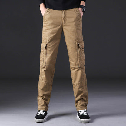 Pantaloni cargo uomo beige, tasche multiple, stile casual, indossati con scarpe sportive nere, sfondo grigio. Moda maschile contemporanea.