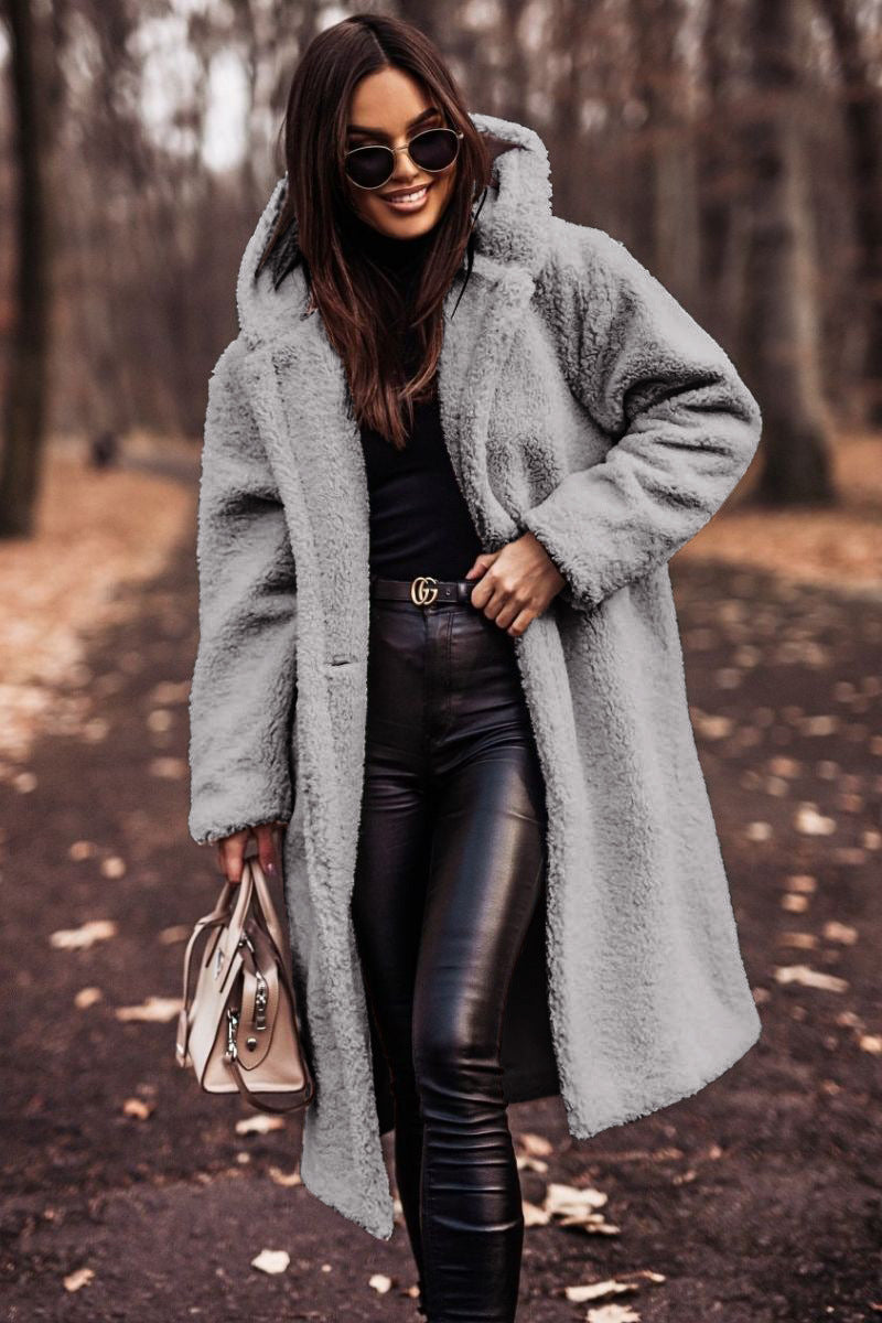 Donna con cappotto teddy grigio, occhiali da sole, pantaloni in pelle nera, borsa beige, cammina in un parco autunnale. Moda autunno inverno.