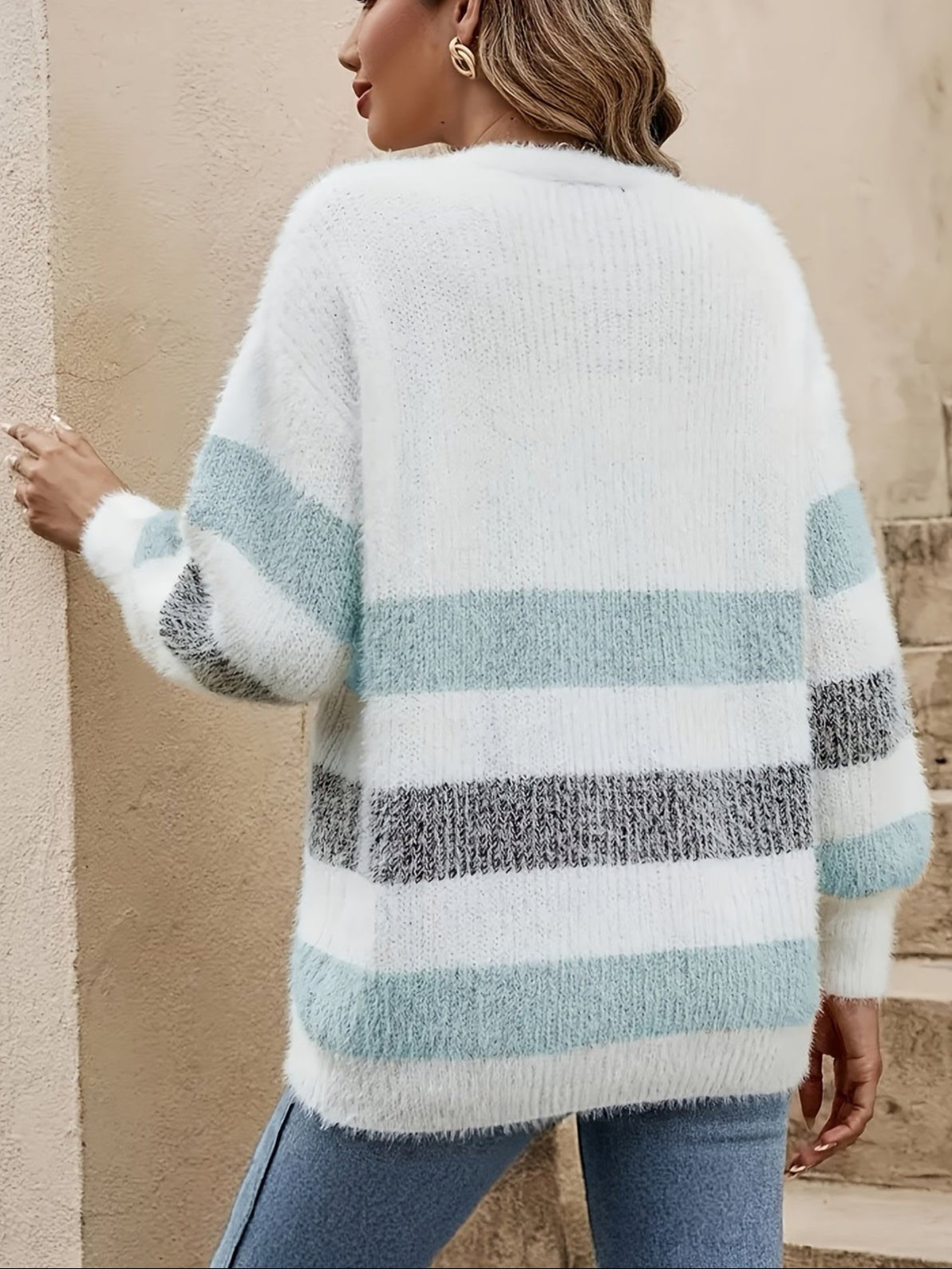 Donna con maglione a righe bianche, azzurre e grigie, in piedi di spalle. Moda autunnale, abbigliamento casual, stile elegante.