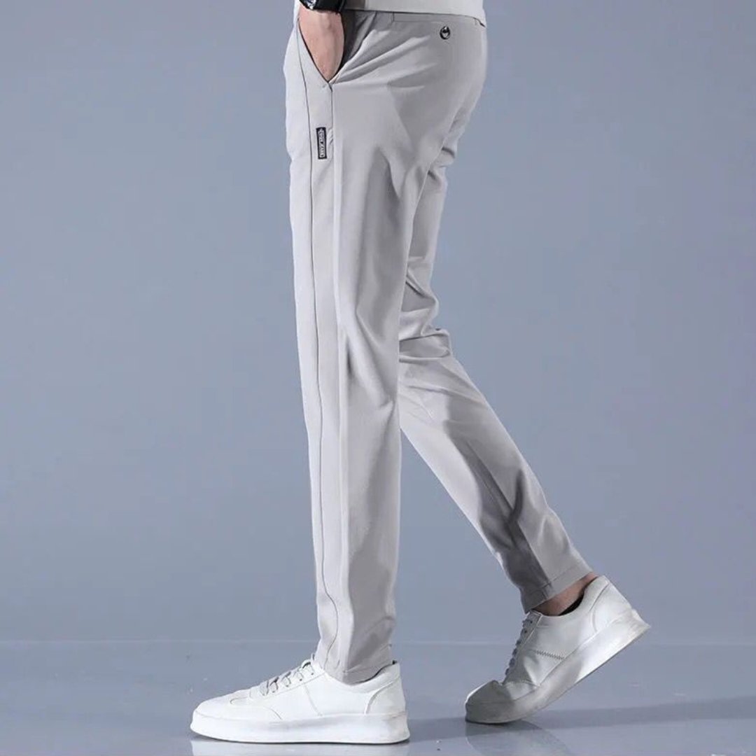 Pantaloni sportivi grigi da uomo, eleganti e comodi, abbinati a scarpe da ginnastica bianche su sfondo grigio. Moda casual maschile.