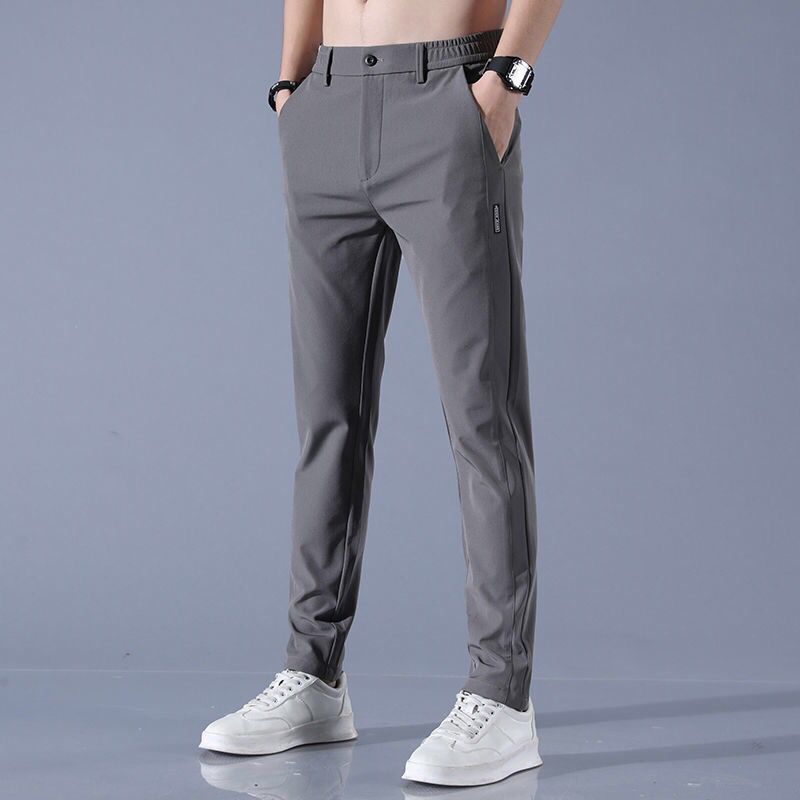 Pantaloni grigi da uomo eleganti, vestibilità slim, con tasche laterali. Indossati con scarpe bianche sportive. Moda maschile casual.