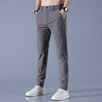 Pantaloni grigi da uomo eleganti, vestibilità slim, con tasche laterali. Indossati con scarpe bianche sportive. Moda maschile casual.