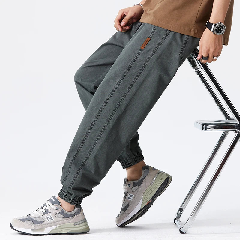 Pantaloni cargo grigi da uomo, stile casual, abbinati a scarpe da ginnastica New Balance, seduto su una sedia moderna. Moda streetwear maschile.