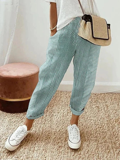Pantaloni a righe verdi e bianche, abbinati a scarpe da ginnastica bianche e borsa a tracolla in paglia. Stile casual estivo femminile.