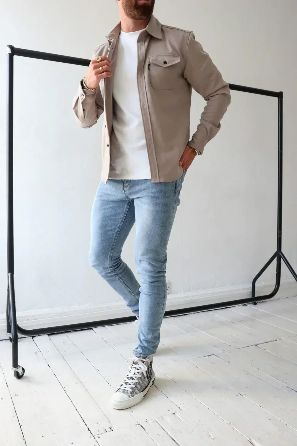 Uomo in jeans attillati e camicia beige, posa casual su pavimento in legno bianco. Moda maschile, abbigliamento casual, stile urbano.