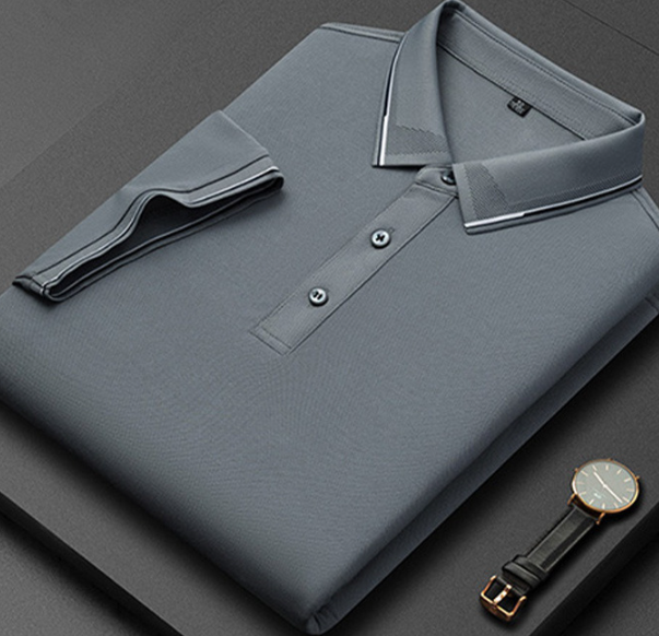Camicia polo grigia piegata su sfondo nero, con colletto a contrasto e bottoni, accanto a un orologio elegante. Moda uomo, abbigliamento casual.