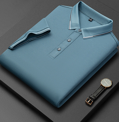 Camicia polo blu piegata su sfondo nero, con dettagli a righe sul colletto e tre bottoni. Orologio da polso elegante con cinturino in pelle accanto.