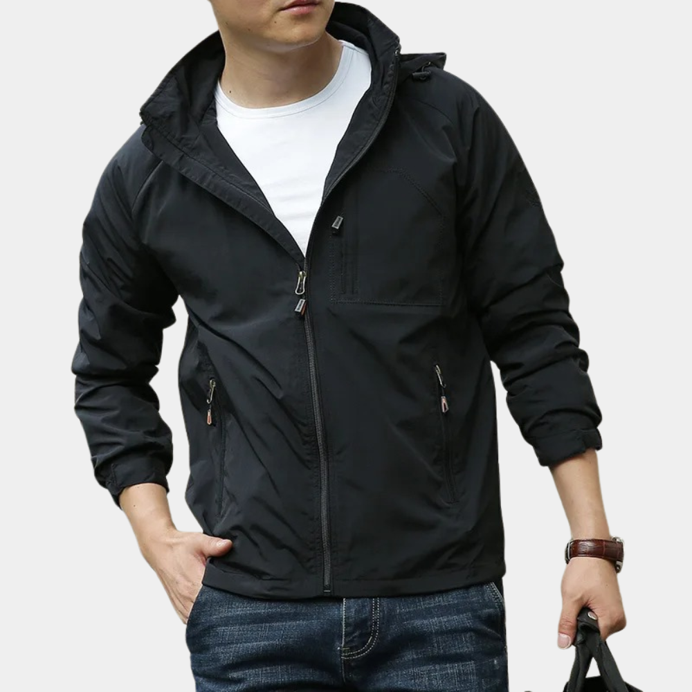 Giacca nera da uomo con cappuccio, zip frontale e tasche, indossata su maglietta bianca e jeans. Moda casual maschile, abbigliamento autunnale.