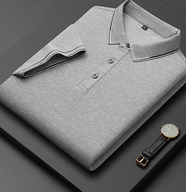 Camicia polo grigia piegata su sfondo nero, con orologio elegante accanto. Moda uomo, abbigliamento casual, stile minimalista.